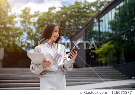 A gorgeous businesswoman is checking messages on her phone while walking down the stairs outdoors. A gorgeous businesswoman is checking messages on her phone while walking down the stairs outdoors. 116075577