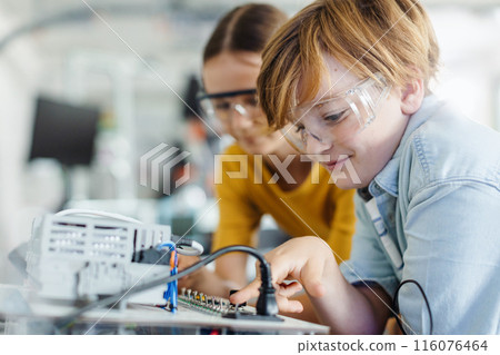 Two classmates working together on circuit board, building robot in after-school robotics club. Children learning robotics in Elementary school. 116076464