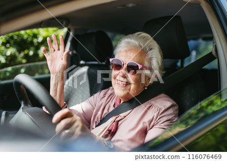 Happy senior woman driving car alone, enjoying car ride. Safe driving for elderly adults, older driver safety. 116076469