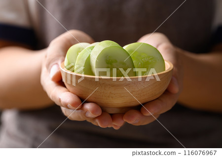 Sliced cucumber in wooden bowl holding by hand, Organic vegetable, Food ingredient 116076967
