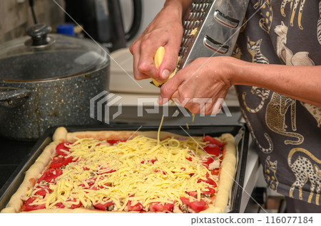 woman prepares pizza with cheese, tomatoes and chicken ham, woman rubs cheese 10 116077184