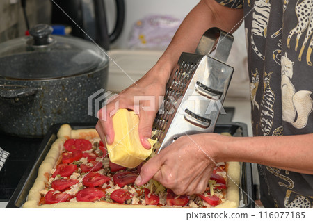 woman prepares pizza with cheese, tomatoes and chicken ham, woman rubs cheese 1 woman prepares pizza with cheese, tomatoes and chicken ham, woman rubs cheese 1 116077185