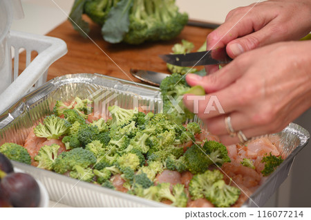 woman cutting broccoli into chicken fillet for baking11 116077214