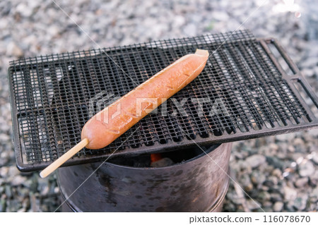 [Solo camping at an auto campsite: grilling frankfurters on a grill] 116078670