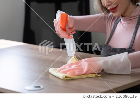 Housekeeper Cleaning a Wooden Table with Spray Bottle and Cloth in Modern Home Environment 116080139