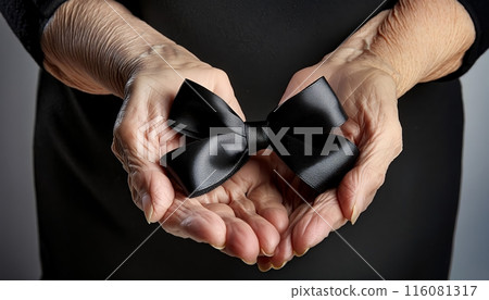 Hands of an elderly person holding a black ribbon in mourning of a deceased person, hands holding black mourning ribbon 116081317
