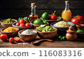 Mexican food ingredients on a rustic table: tomatoes, limes, cheese, guacamole, spices, oil, and juice, creating a colorful and appetizing setup. 116083316