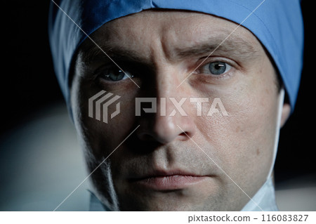Extreme closeup portrait of young male surgeon looking at camera with dramatic light in hospital 116083827