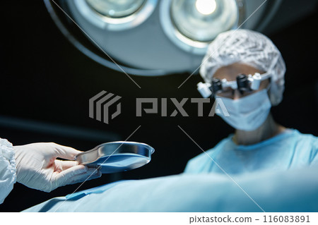 Close up of medical assistant handing dish to female surgeon in operating room with blurred background copy space 116083891