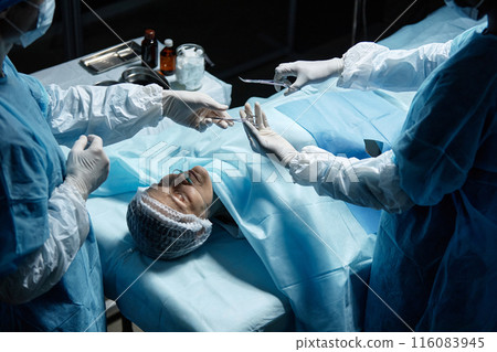 High angle view of female patient under anesthesia lying on operating table with surgeons preparing tools copy space 116083945