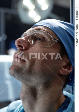 Vertical side view portrait of male surgeon looking up in operating room with dramatic lighting 116083999