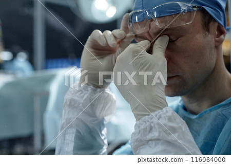 Close up of exhausted male surgeon rubbing eyes during long surgery in operating room copy space Close up of exhausted male surgeon rubbing eyes during long surgery in operating room copy space 116084000