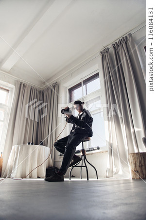 Vertical wide angle view at male photographer holding camera in minimal white photo studio set 116084131
