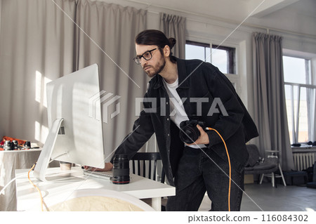 Portrait of young man as photographer using computer in studio in minimal white colors, copy space 116084302