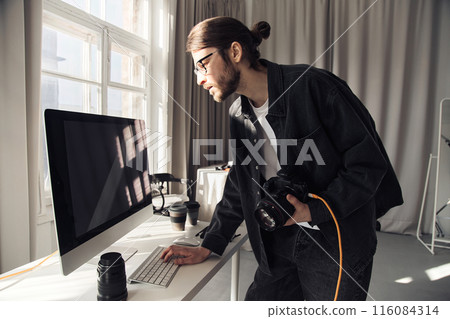 Minimal side view portrait of bearded young man as professional photographer using computer in studio with sunlight accent, copy space Minimal side view portrait of bearded young man as professional photographer using computer in studio with sunlight accent, copy space 116084314