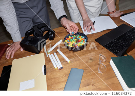 Top view closeup of business team discussing VR project and eating candy snacks at wooden table, shot with flash 116084372