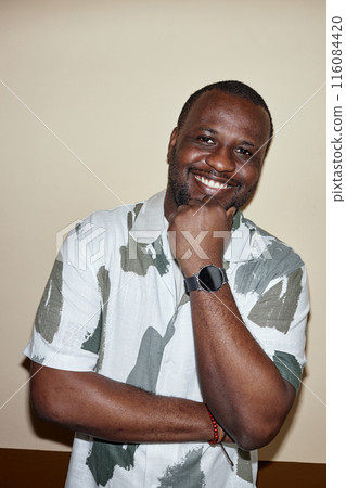 Vertical waist up portrait of smiling Black man looking at camera posing against wall in neutral colors shot with flash Vertical waist up portrait of smiling Black man looking at camera posing against wall in neutral colors shot with flash 116084420