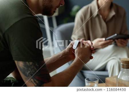 Close up of unrecognizable army veteran holding dog tags necklace in clasped hands during emotional therapy session dealing with grief and PTSD copy space 116084430