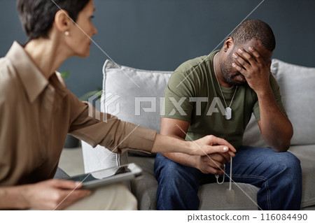 Portrait of struggling army veteran crying in therapy session with female psychologist holding hands and comforting him copy space Portrait of struggling army veteran crying in therapy session with female psychologist holding hands and comforting him copy space 116084490