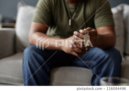 Closeup of African American man as army veteran holding dog tags necklace in hands during therapy session copy space 116084496