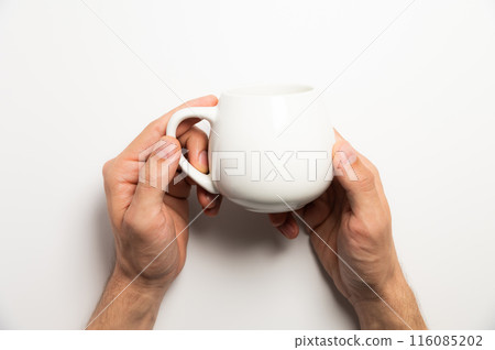 Male hands hold a white mug for tea or coffee on a white background. Studio shot top view 116085202