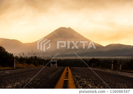 Volcanic Mount Ngauruhoe with golden sky in foggy over highway road at Tongariro national park, New Zealand 116086387