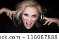 Close-up portrait of a beautiful blonde woman with closed eyes listening to the agressive music via headphones and singing. 116087888