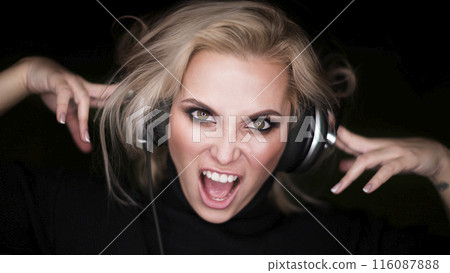 Close-up portrait of a beautiful blonde woman with closed eyes listening to the agressive music via headphones and singing. Close-up portrait of a beautiful blonde woman with closed eyes listening to the agressive music via headphones and singing. 116087888