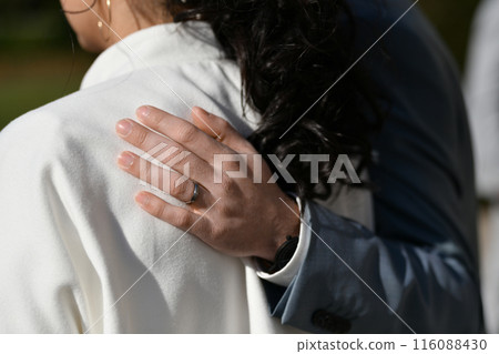 The groom hugs the bride by the shoulder with his hand, which is wearing a wedding ring 116088430