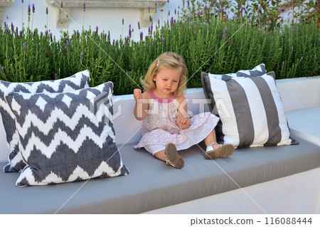 Two year old girl sits on sofa surrounded by lavender 116088444