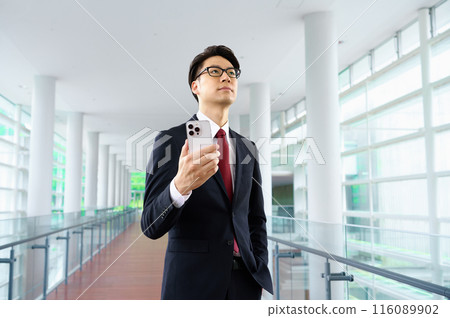 A businessman in a suit walking down a corridor with a smartphone A businessman in a suit walking down a corridor with a smartphone 116089902