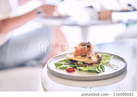 Potato pancakes with herbs, served with slices of lightly salted salmon and sauce. A healthy breakfast. A background of unrecognizable unfocused people with space to copy. High quality photo Potato pancakes with herbs, served with slices of lightly salted salmon and sauce. A healthy breakfast. A background of unrecognizable unfocused people with space to copy. High quality photo 116090082