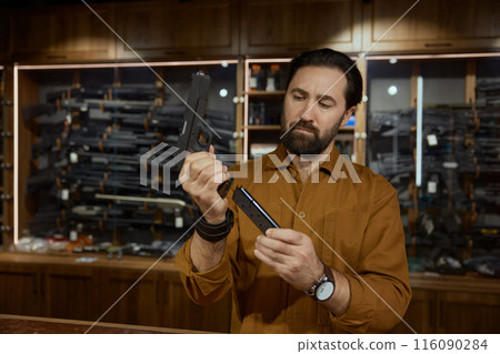 Portrait of salesman charging handgun demonstrating new model for customer 116090284