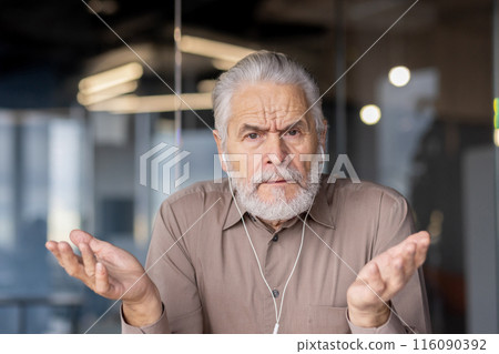 An elderly businessman with a confused expression shrugs his shoulders during a virtual meeting in a modern office. The image captures feelings of uncertainty, workplace communication An elderly businessman with a confused expression shrugs his shoulders during a virtual meeting in a modern office. The image captures feelings of uncertainty, workplace communication 116090392