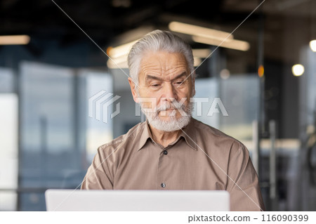 Experienced senior businessman focusing on work on his laptop in a contemporary office setting. Image portrays dedication, professionalism, and concentration, ideal for representations of business 116090399