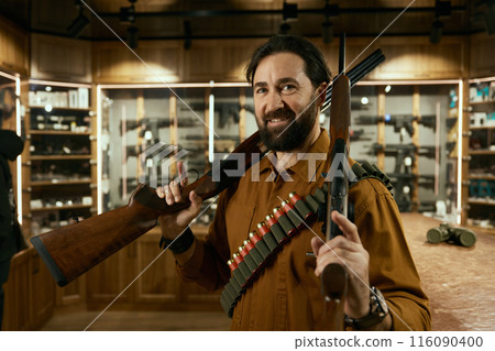 Portrait of hunter at weapon shop standing with rifles 116090400