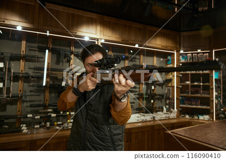 Man entrepreneur checking gun aiming telescopic sight at weapon store 116090410