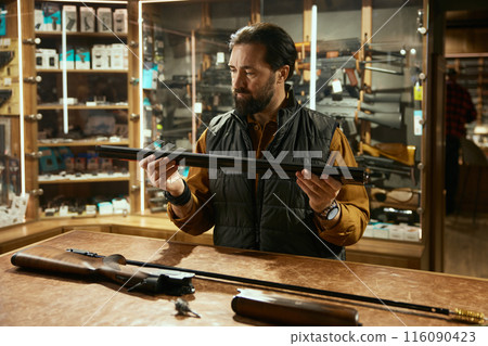 Seller cleaning gun with ramrod while working in hunting shop 116090423