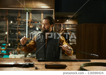 Weapon shop owner cleaning gun with brush preparing goods for sale 116090424