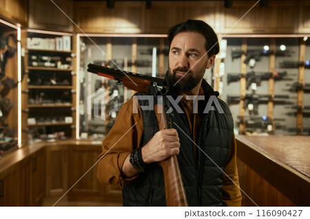 Salesman demonstrating rare collectible hunting rifle over gun shop interior 116090427