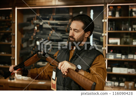 Concentrated salesman checking gun firearm while working at weapon shop 116090428