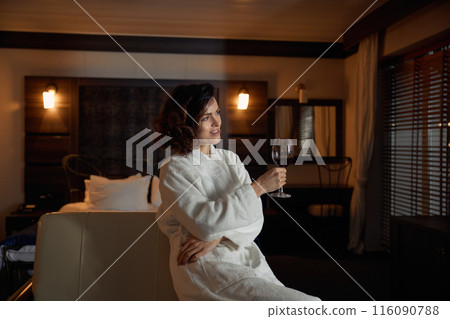 Pretty young businesswoman wearing bathrobe resting with glass of wine 116090788