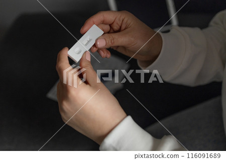Caucasian woman holds nasal swab and puts into nose for COVID-19 self test at home 116091689