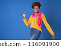Young pretty black woman dancing with afro curly hair smiling in fuchsia scarf and yellow sweater on blue background with copy space. Happiness concept. 116091900