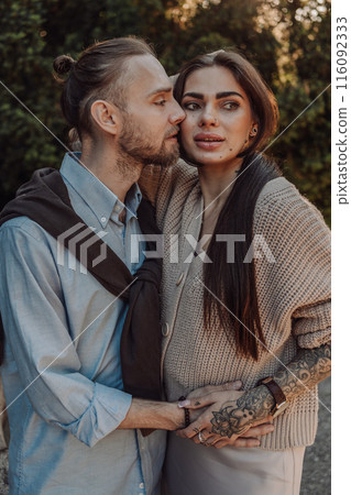 Smiling tattooed girl hugging her boyfriend in a park. Pretty redhead woman with tattoos and man on a walk. 116092333