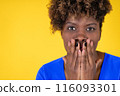 A woman with dark hair and a blue shirt is covering her mouth with her hand 116093301