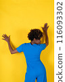 A woman in a blue outfit is leaning against a yellow wall 116093302