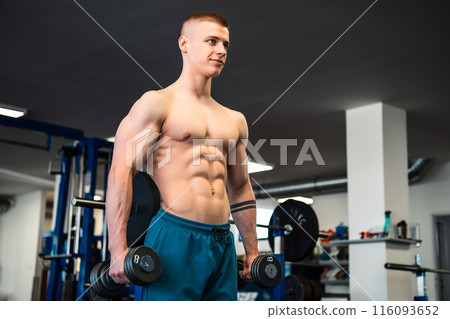 A muscular man lifts weights in a gym during a workout session 116093652