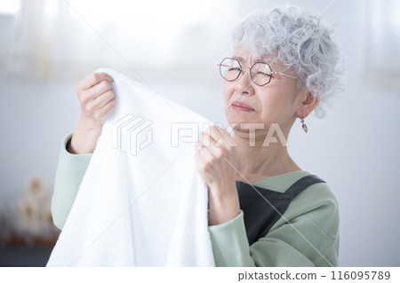 Close-up of a senior (elderly) woman who is troubled by smelly towels after drying laundry indoors during the rainy season Close-up of a senior (elderly) woman who is troubled by smelly towels after drying laundry indoors during the rainy season 116095789