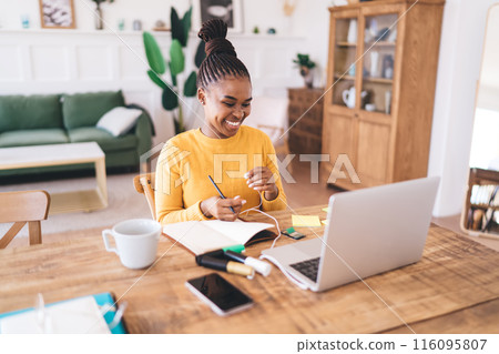 Smiling ethnic woman sitting with laptop in living room Smiling ethnic woman sitting with laptop in living room 116095807
